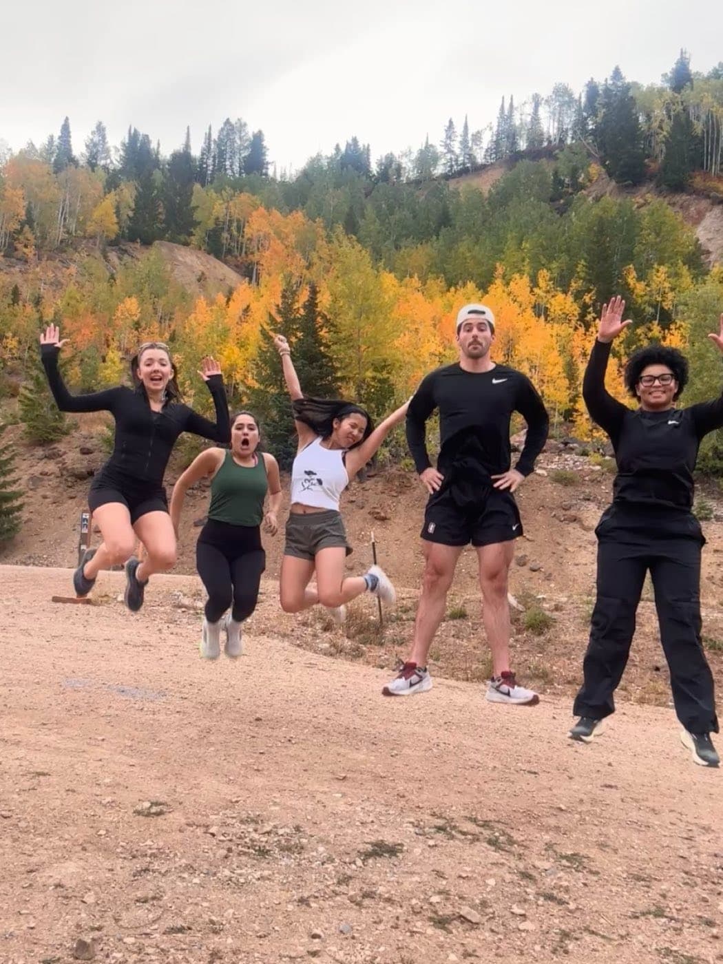 Teammates jumping in the air on a mountain trail during an offsite